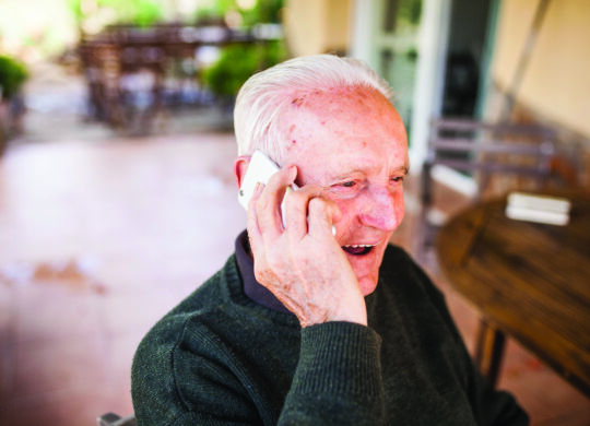 Elderly man talking on the phone on the porch of his house